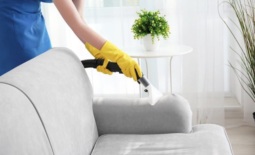 Woman cleaning couch with vacuum cleaner at home